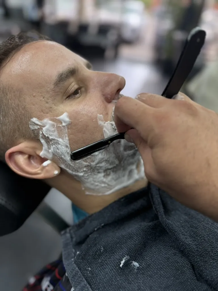 Barber giving a client a hot towel straight razor shave at Wise Guys Barbershop in Denver